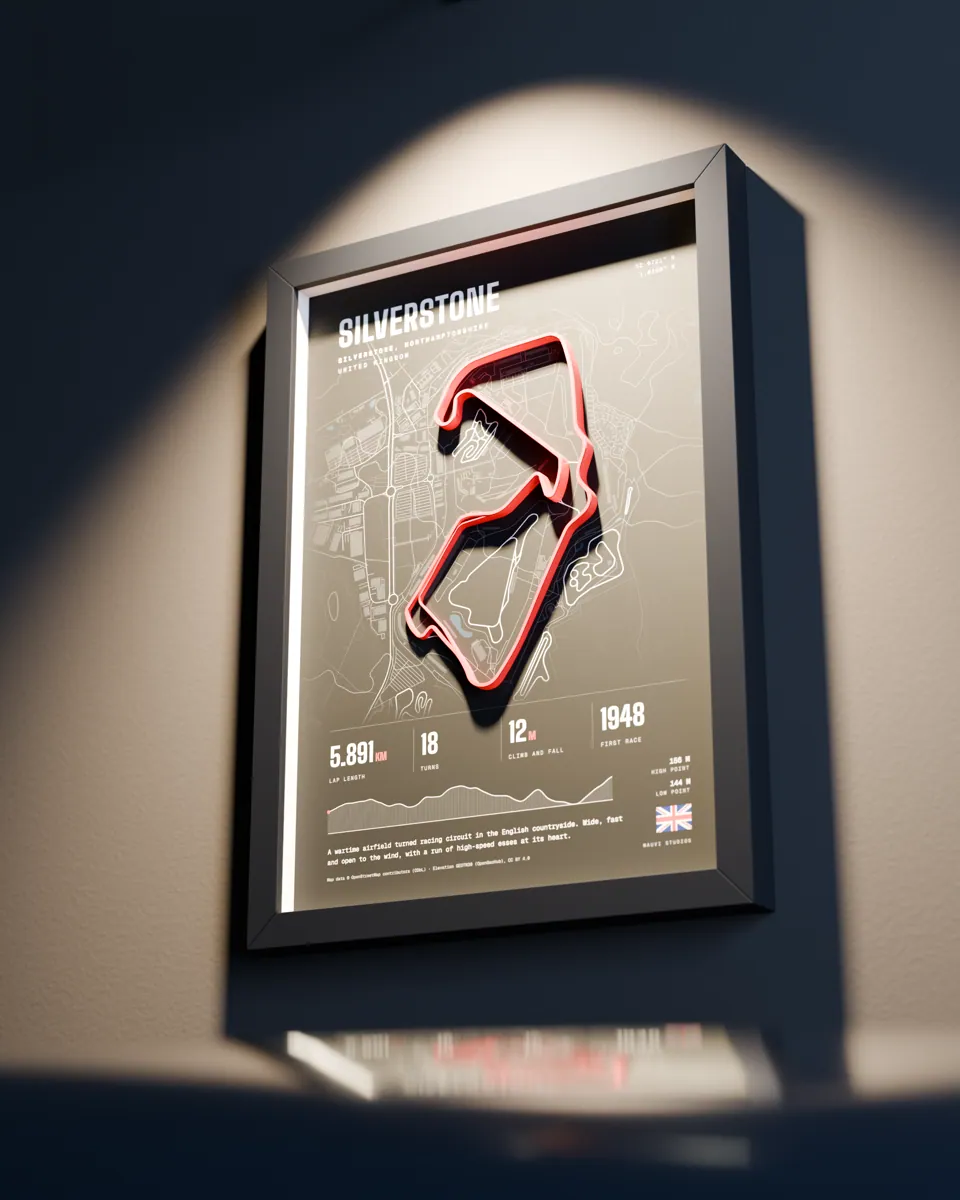 A large framed race-track relief on a den wall, lit by a picture light